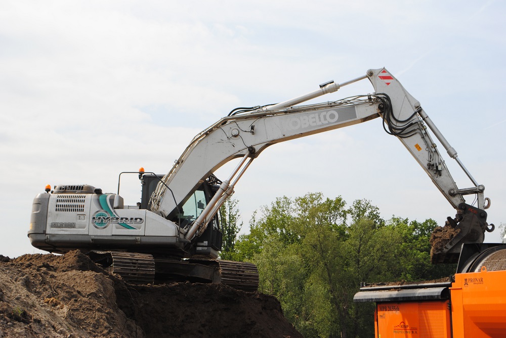 Met de hybride Kobelco wordt de grond met vervuiling in de bak van de zeef gedeponeerd.